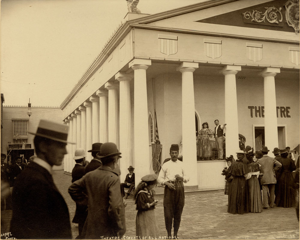 Theater at Streets of All Nations. Performers on stage. Spectators gathered in foreground and in front of stage.