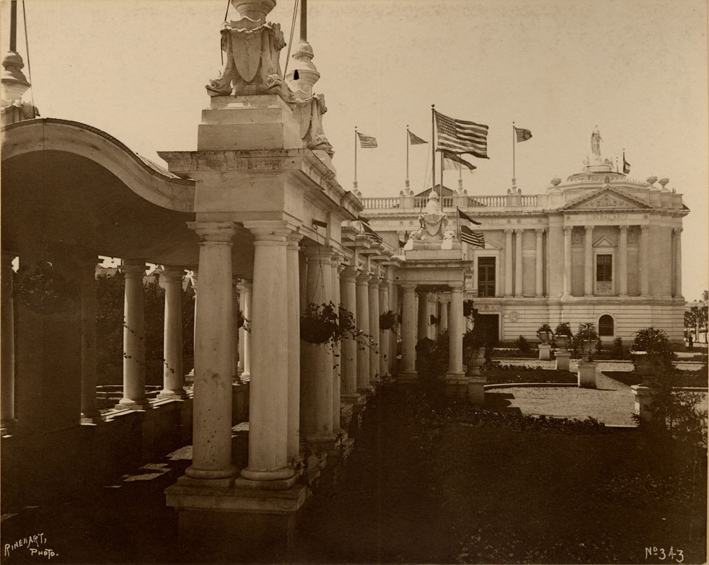 Colonnade and portion of courtyard to east of Liberal Arts building looking west. American Flags mounted on rooftop.