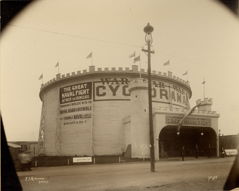 War Cyclorama of the Great Naval Flight attraction on the North Midway. Signage reads: "The Great Naval Flight Between the Iron Clads, Thoroughly replete with the rush, roar & rumble of a terrible naval conflict. Be Patriotic & See it." Three men pose in entryway.