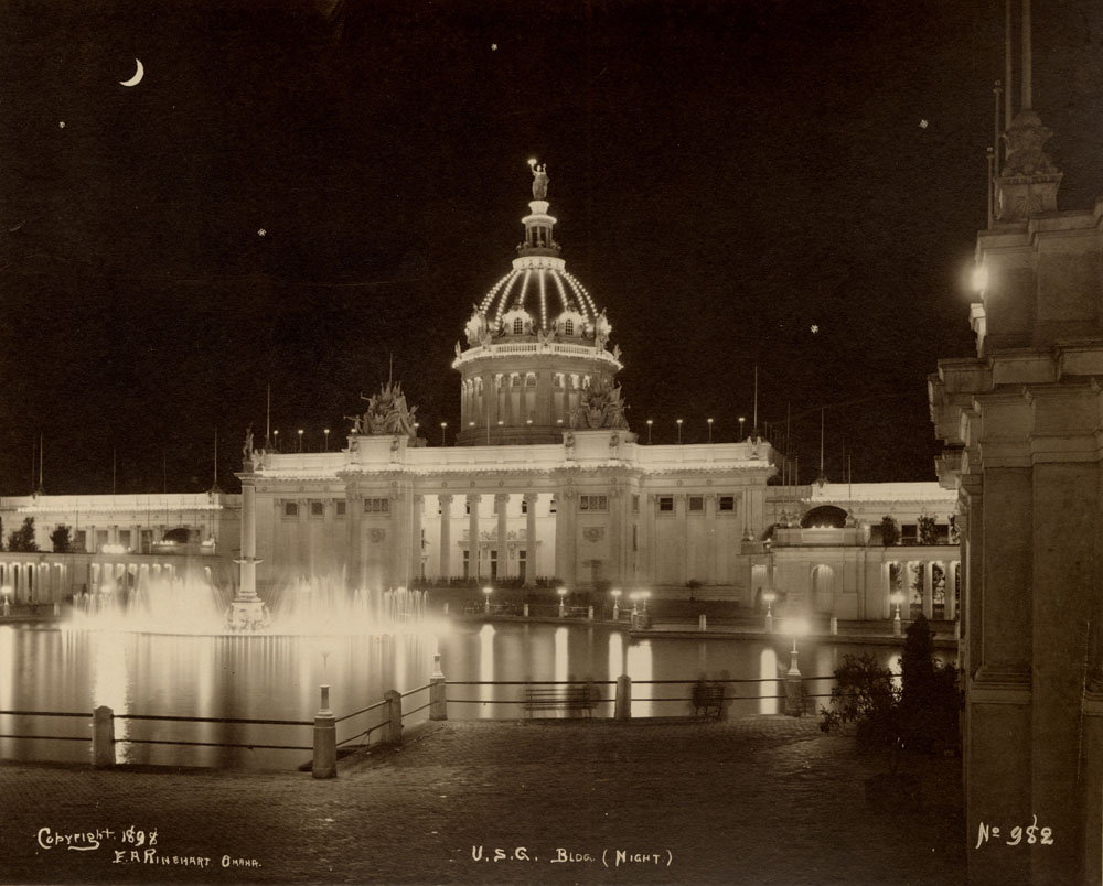 U.S. Government Building at night looking southwest over lagoon. Fountain of Neptune on. Waxing moon and stars in night sky.
