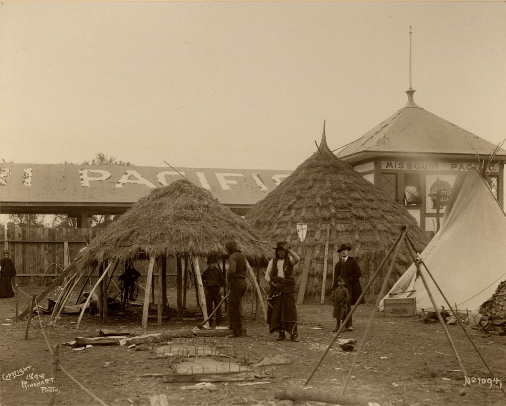 A candid shot three men and two children constructing a thatched wigwam at the Wichita encampment of the Indian Congress.