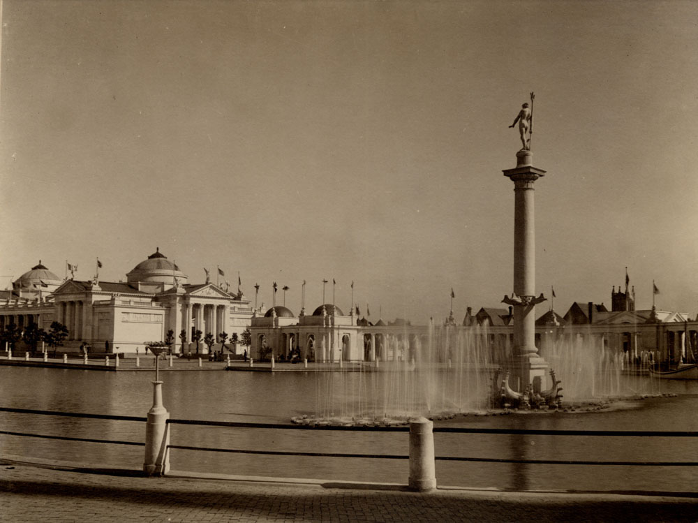 View of Fountain of Neptune, looking southeast across mirror. Fountain turned on. Fine Arts Building and west colonnade visible.