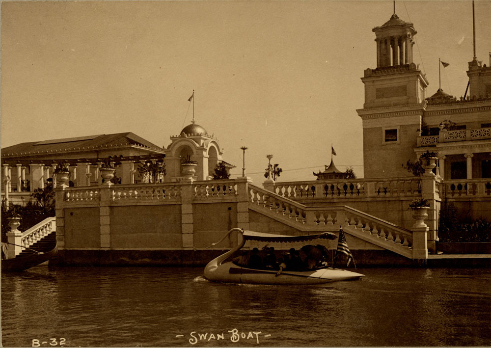 Swan Boat with passengers in lagoon. At base of balustraded staircase in front of Mines and Mining Building. Corner of Mines and Mining Building and southeast portion of Grand Colonnade visible.