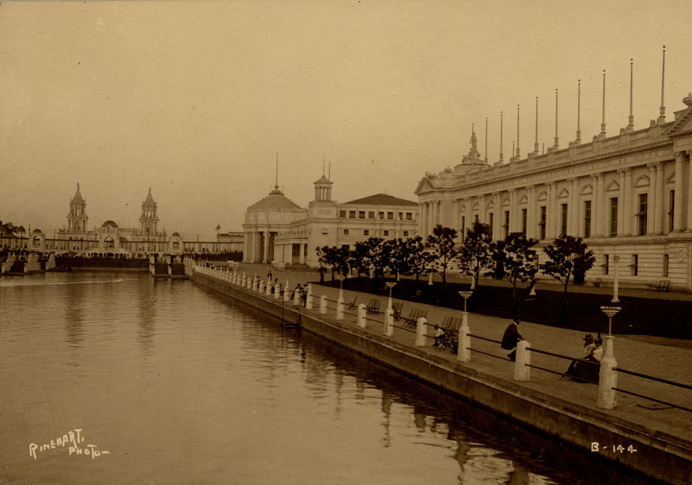 View of lagoon, looking southeast. Grand Colonnade and Twin Towers Restaurants, Mines and Mining Building, and Liberal Arts Building visible. A few people seated on benches surrounding lagoon. Man sits on railing.