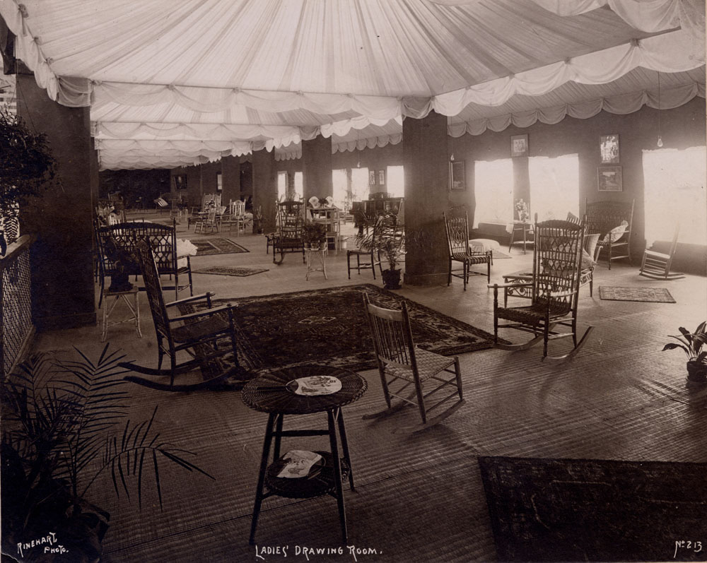 Ladies' Drawing Room in Mines and Mining Building. Room furnished with rocking chairs, straight chairs, desks, side tables, potted plants, and woven rugs.