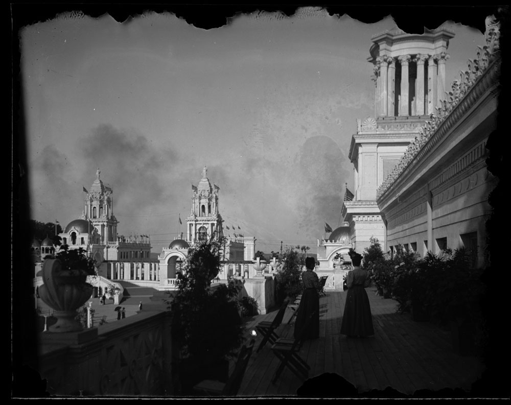 Two women standing on balcony of Mines and Mining Building. View of Twin Towers Restaurants behind Grand Colonnade to the northeast.