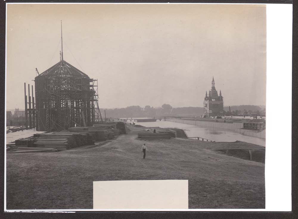 Construction of Mines and Mining Building. Administration Arch to the northwest, across lagoon. People walking. Building materials in foreground.