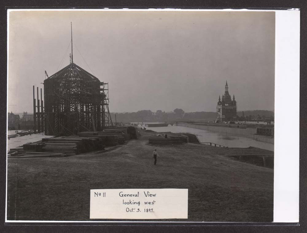 Construction of Mines and Mining Building. Administration Arch to the northwest, across lagoon. People walking. Building materials in foreground.