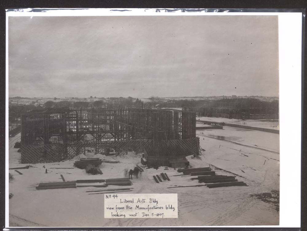 Construction of Liberal Arts Building. Horse and carriage and building materials in foreground. Snow covers ground. Construction of Agriculture Building to the northwest, across lagoon.