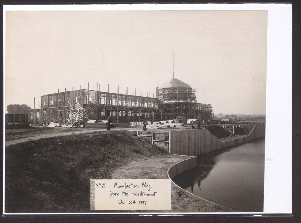 View of Mines and Mining Building construction, looking southeast. East end of lagoon and retaining wall in foreground.