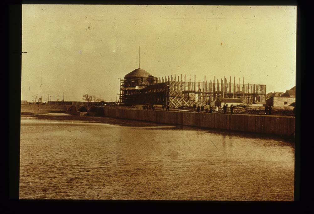 Construction of Mines and Mining Building. Water in lagoon. People stand along top of lagoon retaining wall.