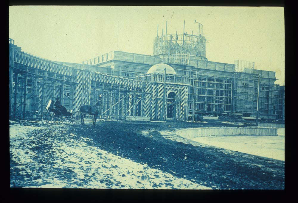 Construction of U.S. Government Building. Horse drawn carriage in front of structure. Retaining wall of lagoon visible.