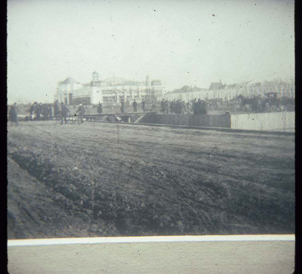 Construction of Mines and Mining Building. Crowd, bicyclists, and horse drawn carriages on both sides of empty lagoon.